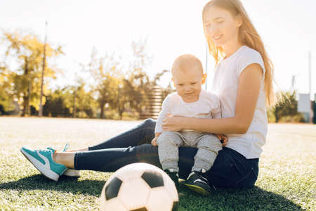 Happy young mom with son playing with soccer ball on field, outdoorsの写真素材