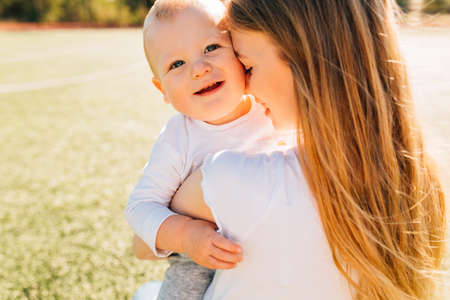 Happy mother kisses and hugs her baby in the park on a summer sunny day, mother's day