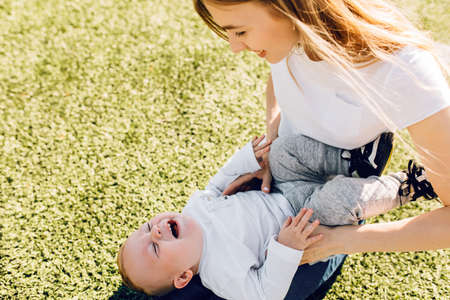 Happy young mom playing and having fun with her little son on the grass in the park, Happy family...