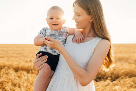 Beautiful young mother with a baby in a wheat field, Happy family in the rays of the sunset, Mother's Dayの写真素材
