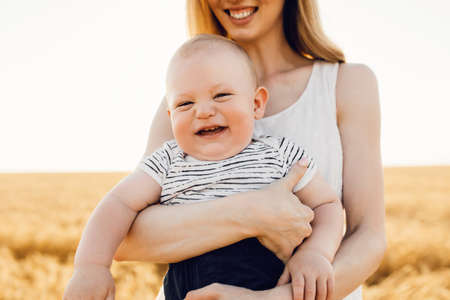 Happy beautiful mother with her baby on the golden wheat field, family on the grain field, mom hugs her little boyの写真素材