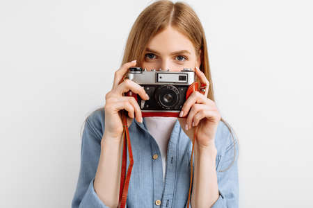 Smiling beautiful young woman taking photo on retro camera isolated on white background