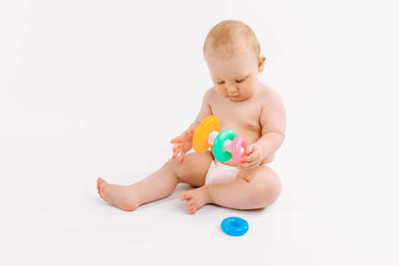 Little baby in a diaper playing with a children's multi-colored developing pyramid on an isolated...