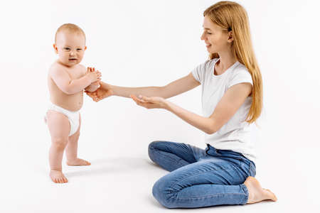 Little child taking the first steps, Happy little child learning to walk with the help of the mother, on a white background, The concept of the growth and development of the childの写真素材