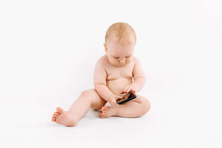 Little baby in a diaper, with a mobile phone sits on an isolated white backgroundの写真素材