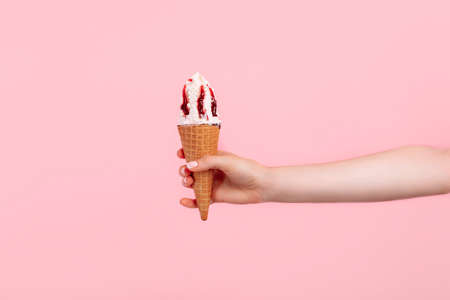 Hand holds strawberry ice cream cone on pink isolated background, Strawberry ice cream in waffle cupの写真素材