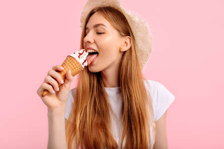 Charming young woman, in a summer hat, with delicious ice cream on a pink backgroundの写真素材
