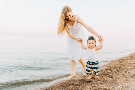 Mother and her little son are having fun on the coast, Young beautiful mother and her baby are playing near the water on the beachの写真素材