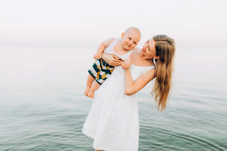 Happy family, young beautiful mother and her baby are having fun on the beach on a summer sunny dayの写真素材