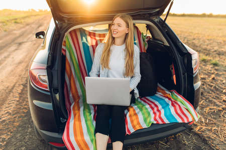 Travel and technology. Happy young woman working on laptop celebrating victory while sitting in...
