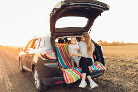 Happy family, a young mother with a child sitting in the trunk of a car, traveling togetherの写真素材