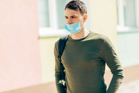 Portrait of a young man in a mask, against the background of a hospital building, outdoors