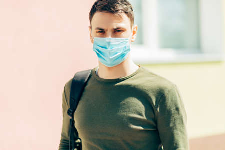 Portrait of a young man in a mask, against the background of a hospital building, outdoorsの写真素材