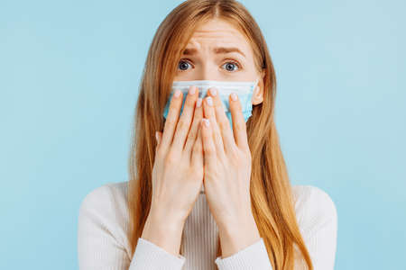 Excited young woman looking wide eyes at camera covering mouth with hands on isolated blue studio...