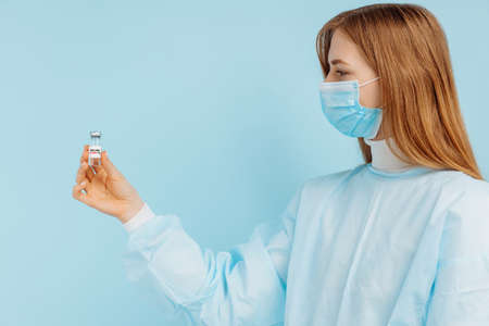 Doctor woman in a medical mask on her face, holds a vaccine against influenza, measles, coronavirus...
