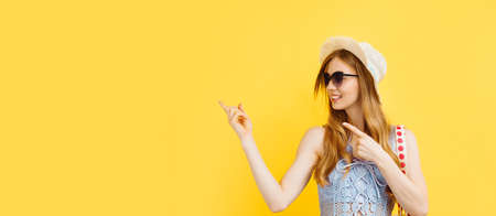 Young surprised young woman, in a summer hat, pointing and looking to the left at a logo, showing an advertisement, on a yellow background.の写真素材