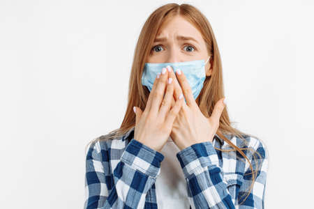 Portrait of shocked young woman in protective mask looking at camera covering her mouth with hand, on white backgroundの写真素材
