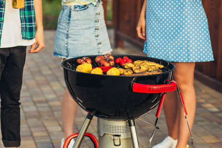 Man making barbecue, assorted vegetables and chicken wings with sausages, grilling on a portable barbecue outdoors in a park in natureの写真素材