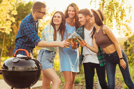 Group of young happy friends having barbecue party in nature, friends fry meat, chat and drink lemonade outdoors in summerの写真素材