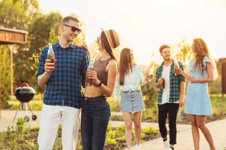 Happy young students walking together outdoors in a summer park, a group of young people walking outdoors and drinking drinks at sunsetの写真素材