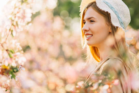Spring romantic image of tender young woman, in hat, happy smiling woman with spring flowers in the garden, spring conceptの写真素材