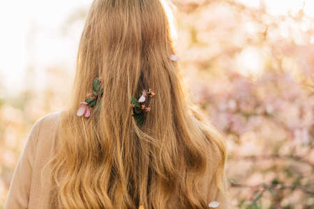 Cute young woman, in a delicate vintage dress, standing next to the colorful pink flowers of trees, romantic womenの写真素材