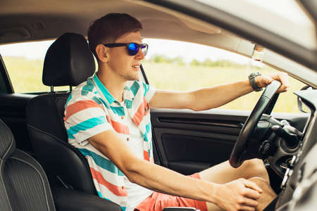 Young man in sunglasses driving his car, happy man driving a car, concept of vacation, trip, travelの写真素材