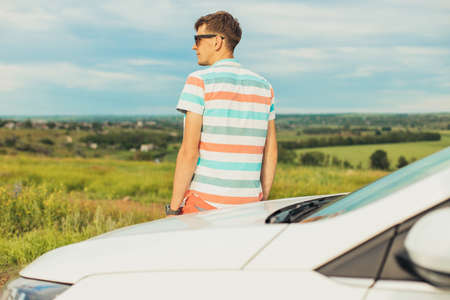 Young male traveler enjoying the beautiful landscape while driving his car, a man standing near his carの写真素材