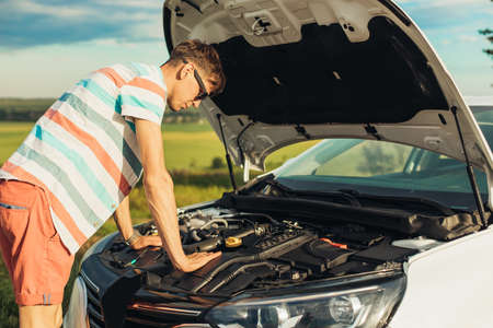 Breakdown of the car. Concentrated young man holding on to the hood of a car and looking inside...