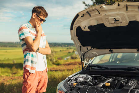 Breakdown of the car. Concentrated young man holding on to the hood of a car and looking inside...