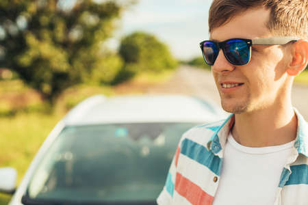 Happy confident young man, in sunglasses, enjoying beautiful nature, standing near his car, Summer vacation concept, tourism, travelの写真素材