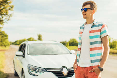 Happy confident young man, in sunglasses, standing near his car, on a summer sunny day on the road, Summer vacation conceptの写真素材