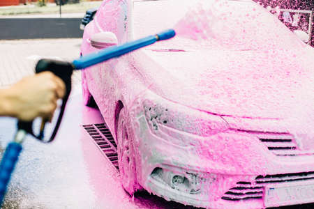 Manual car wash with pressurized water in car washes, a person washes the foam from the car with high pressure waterの写真素材