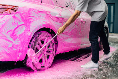 Man worker washes alloy rims of a car at a car wash, a man washes car rims with pink foam and a brushの写真素材