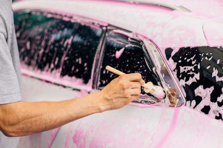 Man worker washes alloy rims of a car at a car wash, a man washes car rims with pink foam and a brushの写真素材