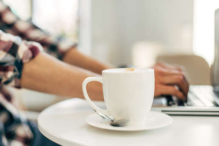 Close up image of male hands working and typing on a laptop keyboard with a cup of coffee on a wooden table, Man working from home.の写真素材