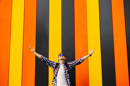 Portrait of happy young man in sunglasses and hat, hipster with raised arms up, excited man with...