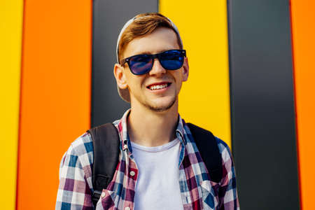 Young happy smiling guy in sunglasses and a cap looking to the side posing while standing against a...