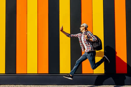 Photo of cheerful positive excited running jumping hipster with briefcase talking on mobile phone...