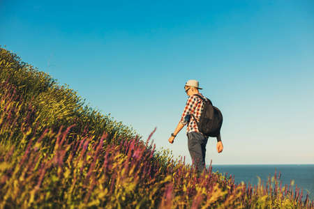 Young man, in shirt and glasses, goes on a hike, with a backpack, Smiling man goes uphill, travel...