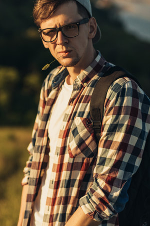 Portrait of a young handsome man, wearing glasses and a cap, smiling young man, standing on the street in nature, against the background of a beautiful forestの写真素材