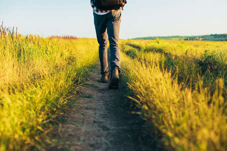 Active tourist, a man with a briefcase in nature, a hipster in a cap is walking along a path on a green hill, healthy lifestyle, nature, restの写真素材