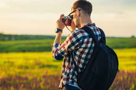 Tourist man in the mountains at sunset, a man with a backpack photographs the sunrise, hipster with...