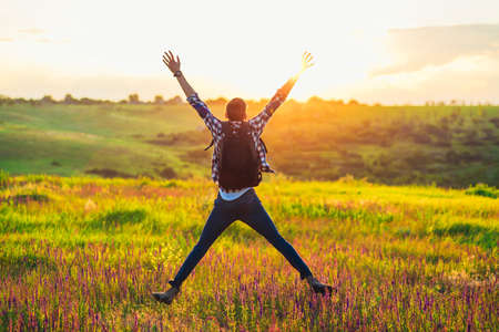Traveler with raised hands standing on a hill in green grass and enjoying a majestic sunset, Successful man enjoying triumph, Concept of sport and success, travelの写真素材