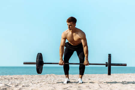 Healthy handsome active man with fit muscular body, young muscular man lifting weights, doing exercises, Sporty man exercising on the beach, Outdoor training, Sport and fitness conceptの写真素材