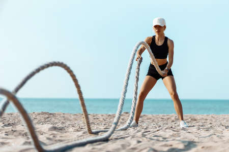 Sporty young woman training with a battle rope, Man doing fitness workout on the beach on a sunny day using two battle ropes on the beachの写真素材