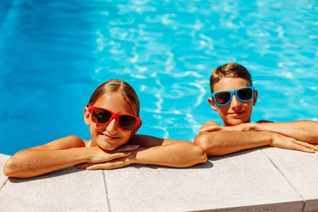 Happy kids in the pool, Funny kids in sunglasses playing outdoors, little boy and girl swim in the pool on a summer sunny day, Summer holiday conceptの写真素材