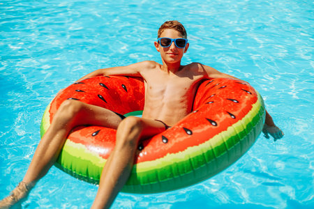 Happy little boy swims with colorful inflatable ring in outdoor pool on hot summer day, Kids toys with water, Kids play in tropical resort, Family beach vacationの写真素材