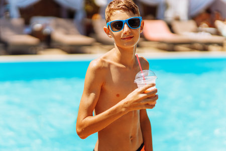 Portrait of a happy boy in sunglasses having a drink near the pool, child with a fresh drink in a luxury pool looking at the camera, summer vacation conceptの写真素材