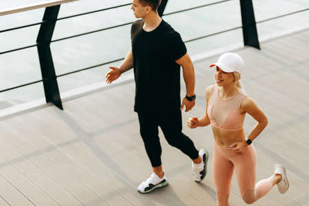 Young sports fitness couple running along the promenade in sportswear, man and woman running sprint outdoors at the seaの写真素材